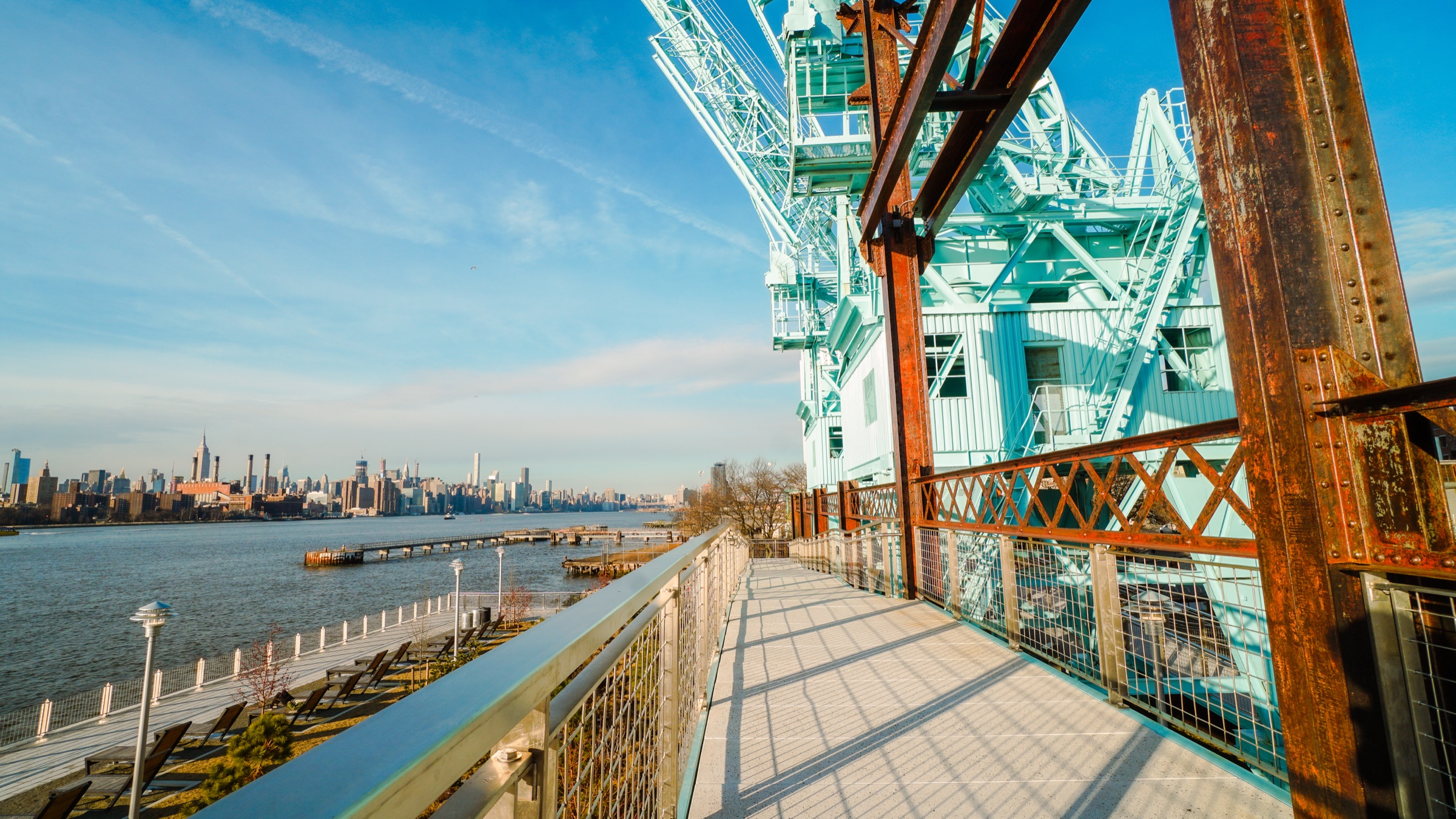 Domino Park's elevated walkway and salvaged refinery cranes along the East River, Williamsburg Bridge beyond