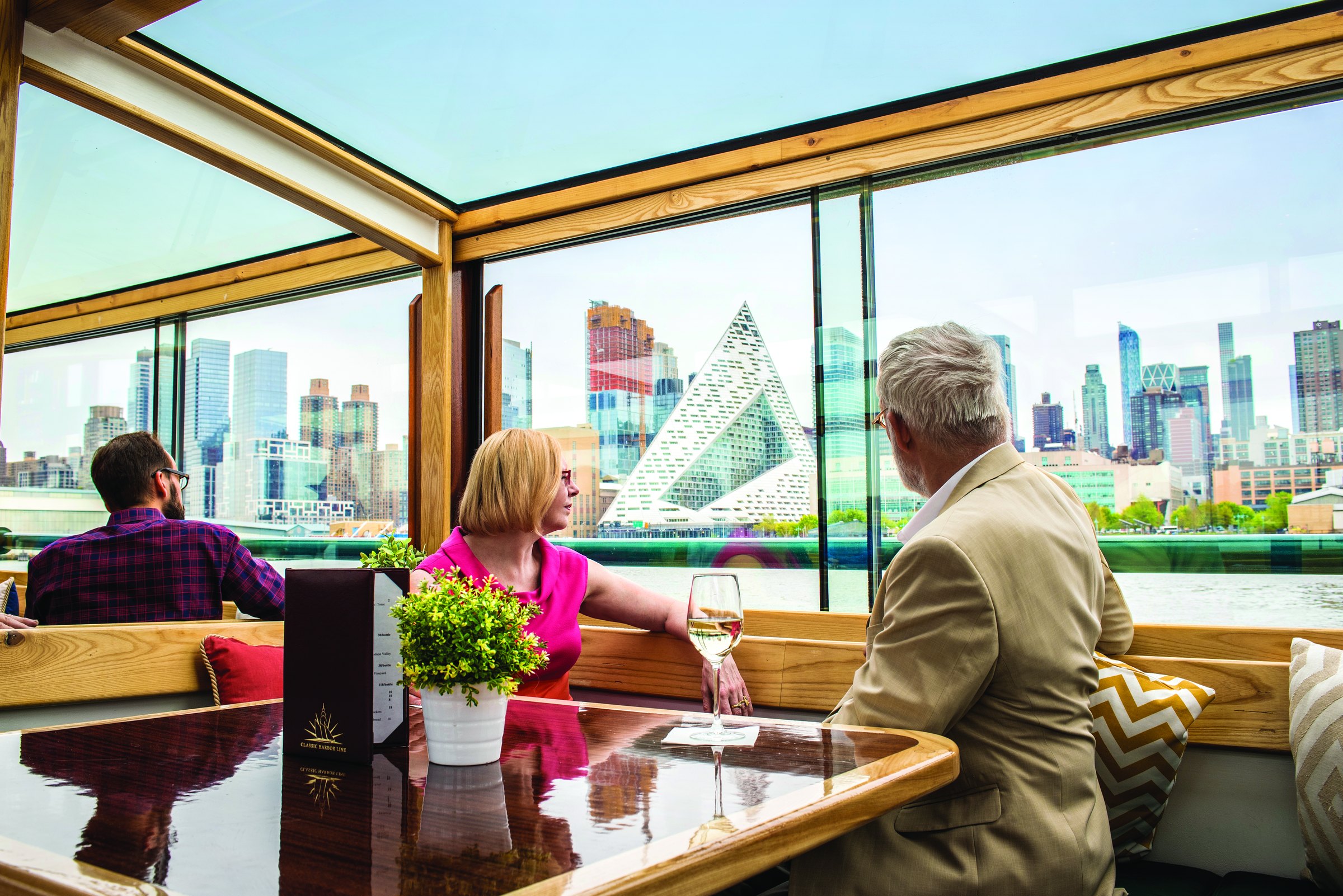 Passengers at a window table aboard a Classic Harbor Line yacht, the Manhattan skyline sliding by