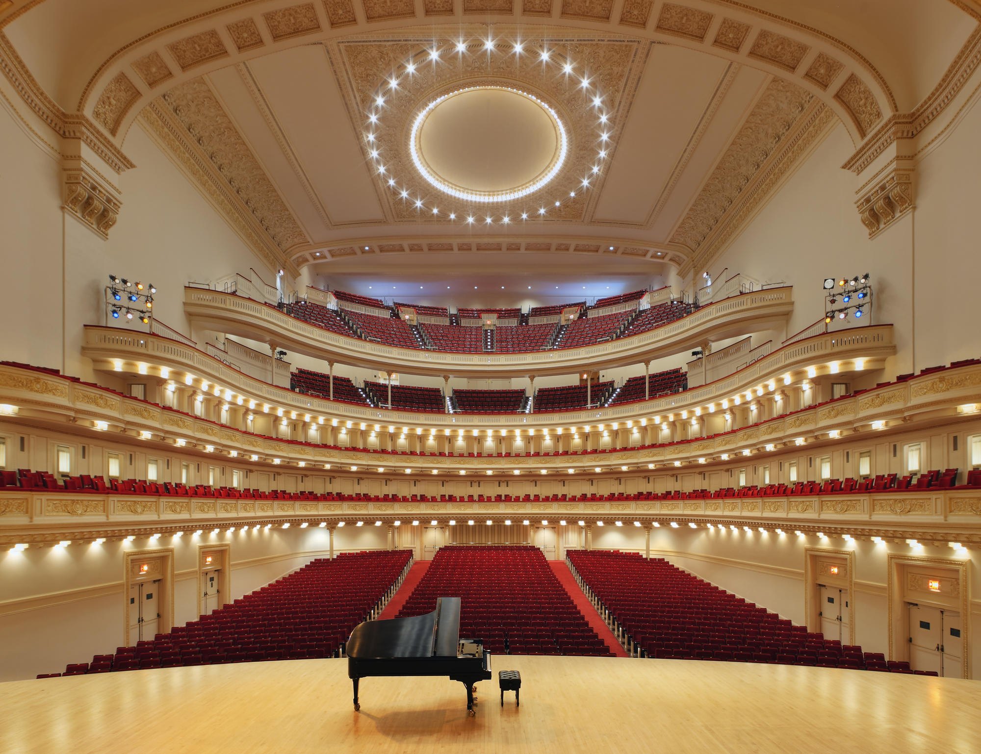 Stern Auditorium at Carnegie Hall seen from the stage, a grand piano in front of the red seats and five gilded tiers rising to the oval ceiling
