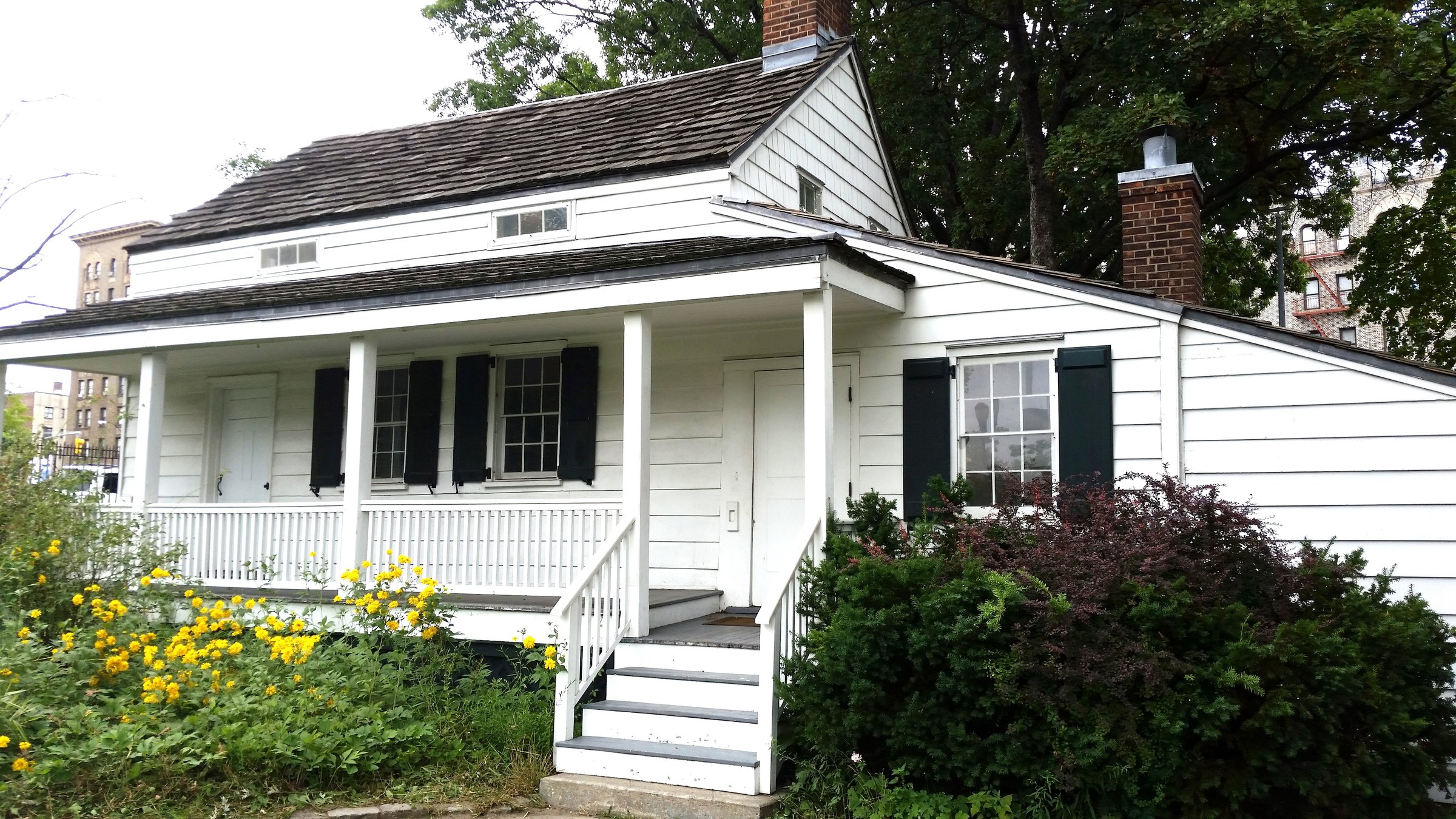 The white clapboard Edgar Allan Poe Cottage in Poe Park on the Grand Concourse, its porch edged with flowers