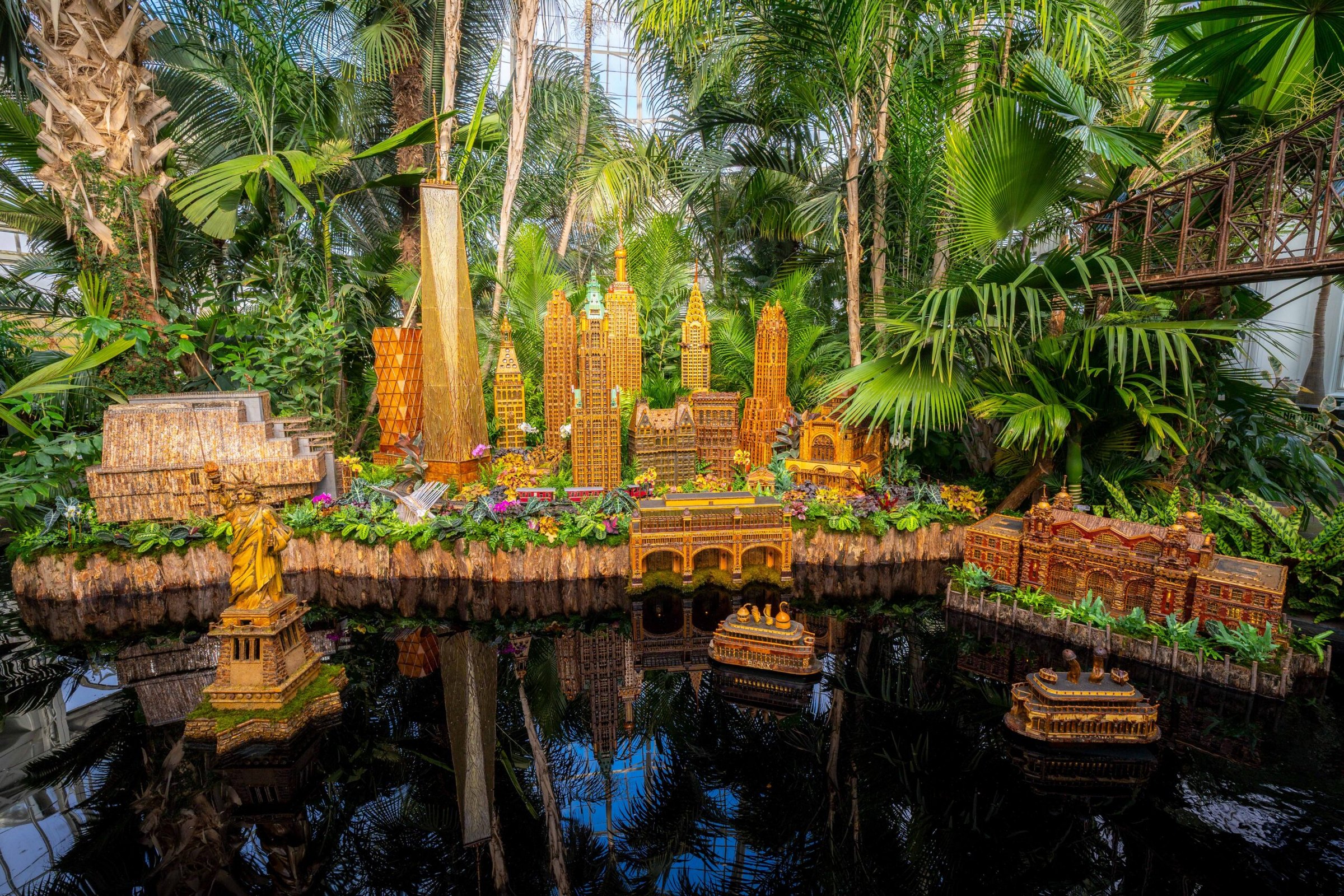 A New York skyline built from bark, seeds and leaves over a reflecting pool in the Haupt Conservatory at the Holiday Train Show