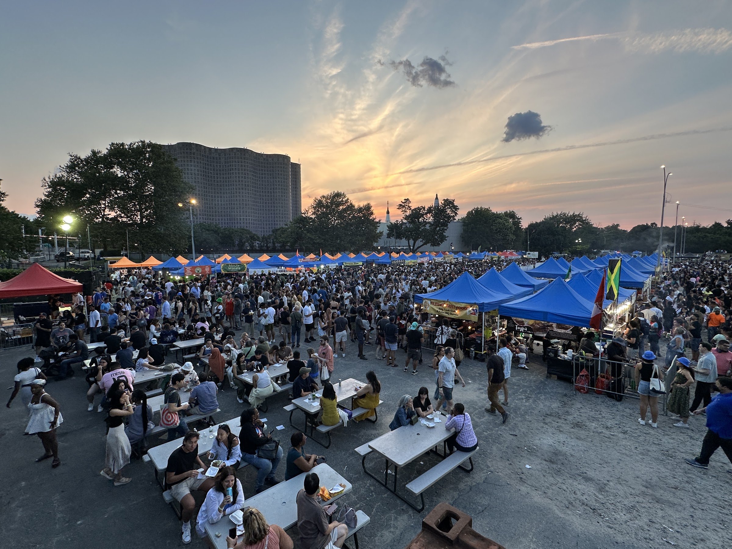 Crowds at the long tables of the Queens Night Market at sunset in Flushing Meadows Corona Park