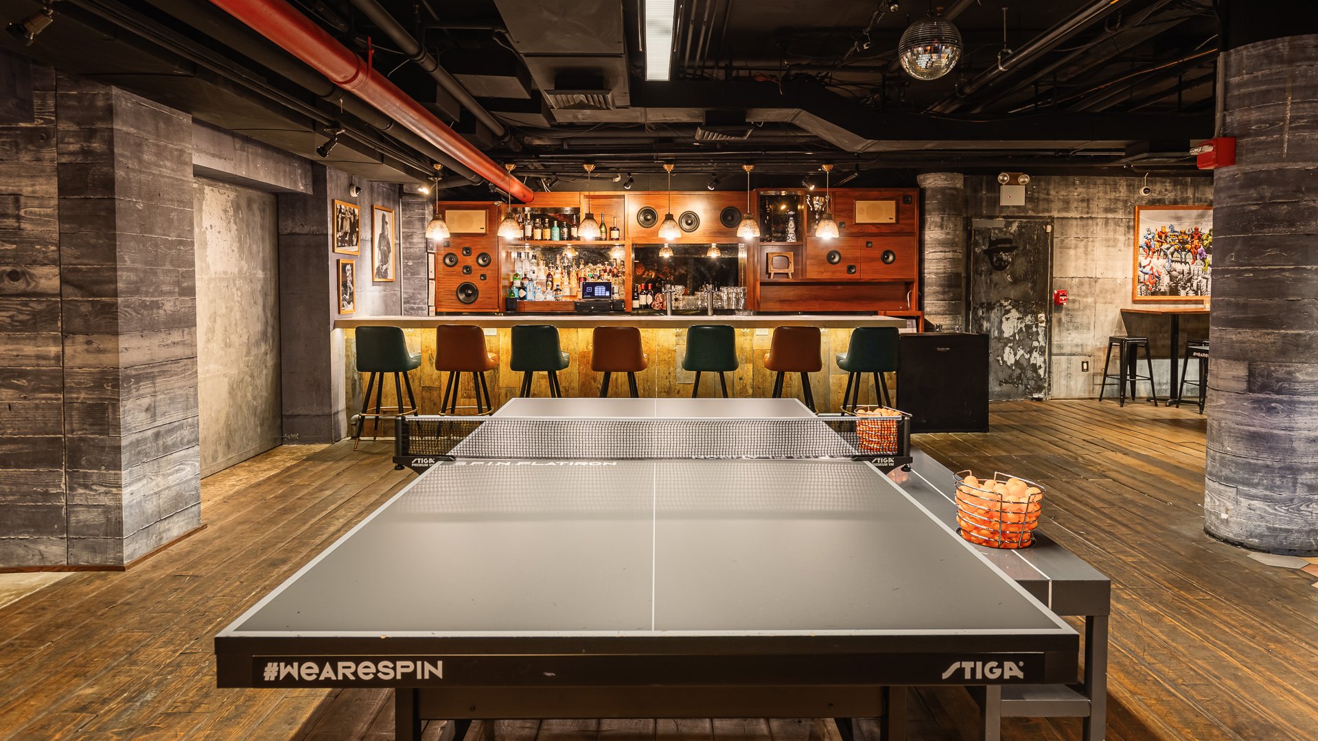 A ping-pong table in the wood-paneled hall at SPIN New York Flatiron, the bar glowing behind