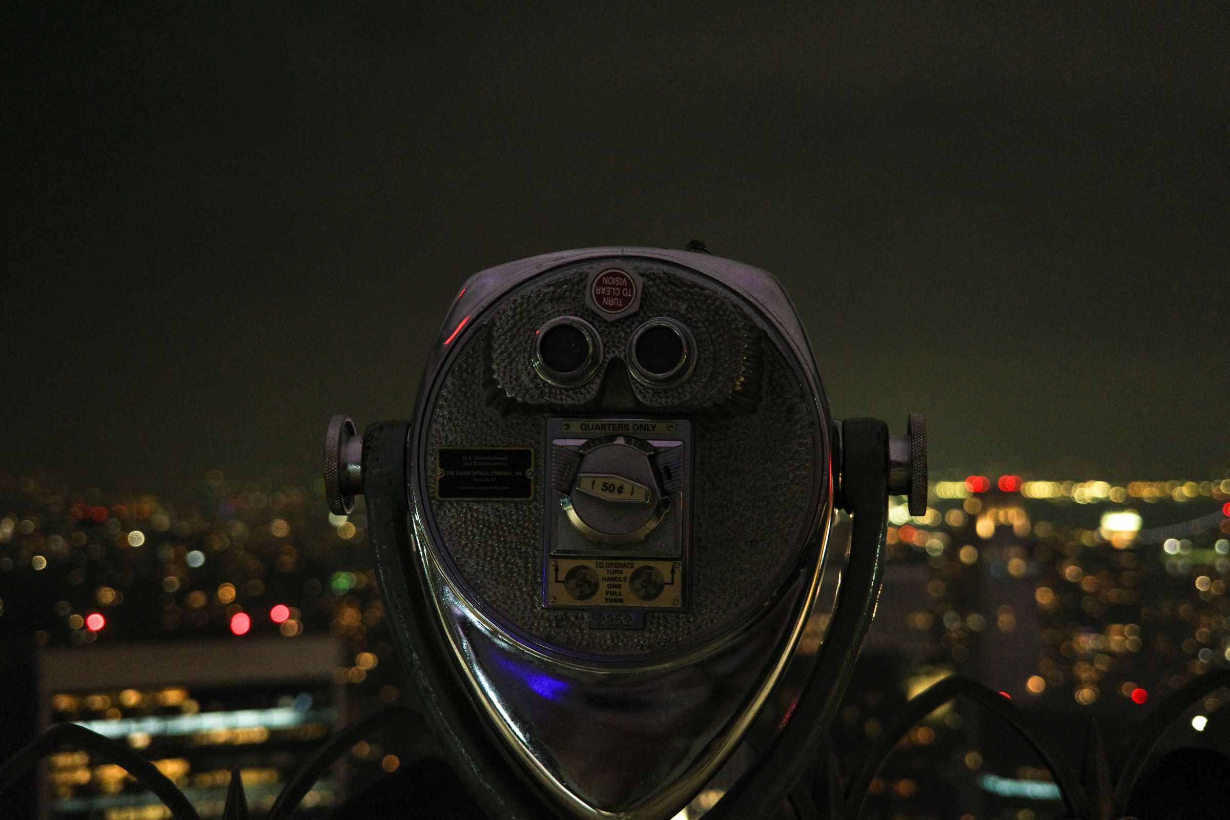 A coin-operated viewer above city lights at night