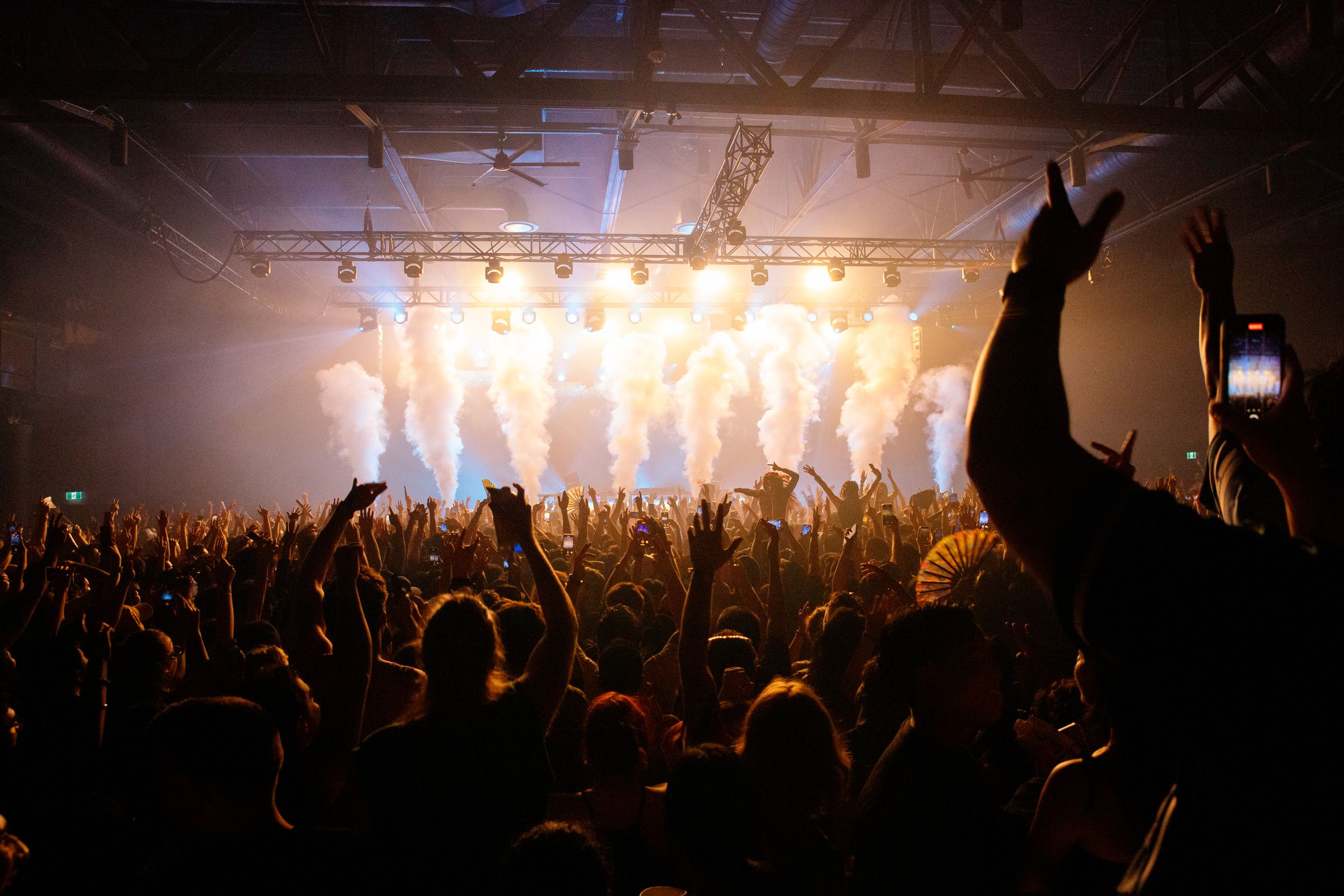 A crowd with raised hands in front of a lit stage