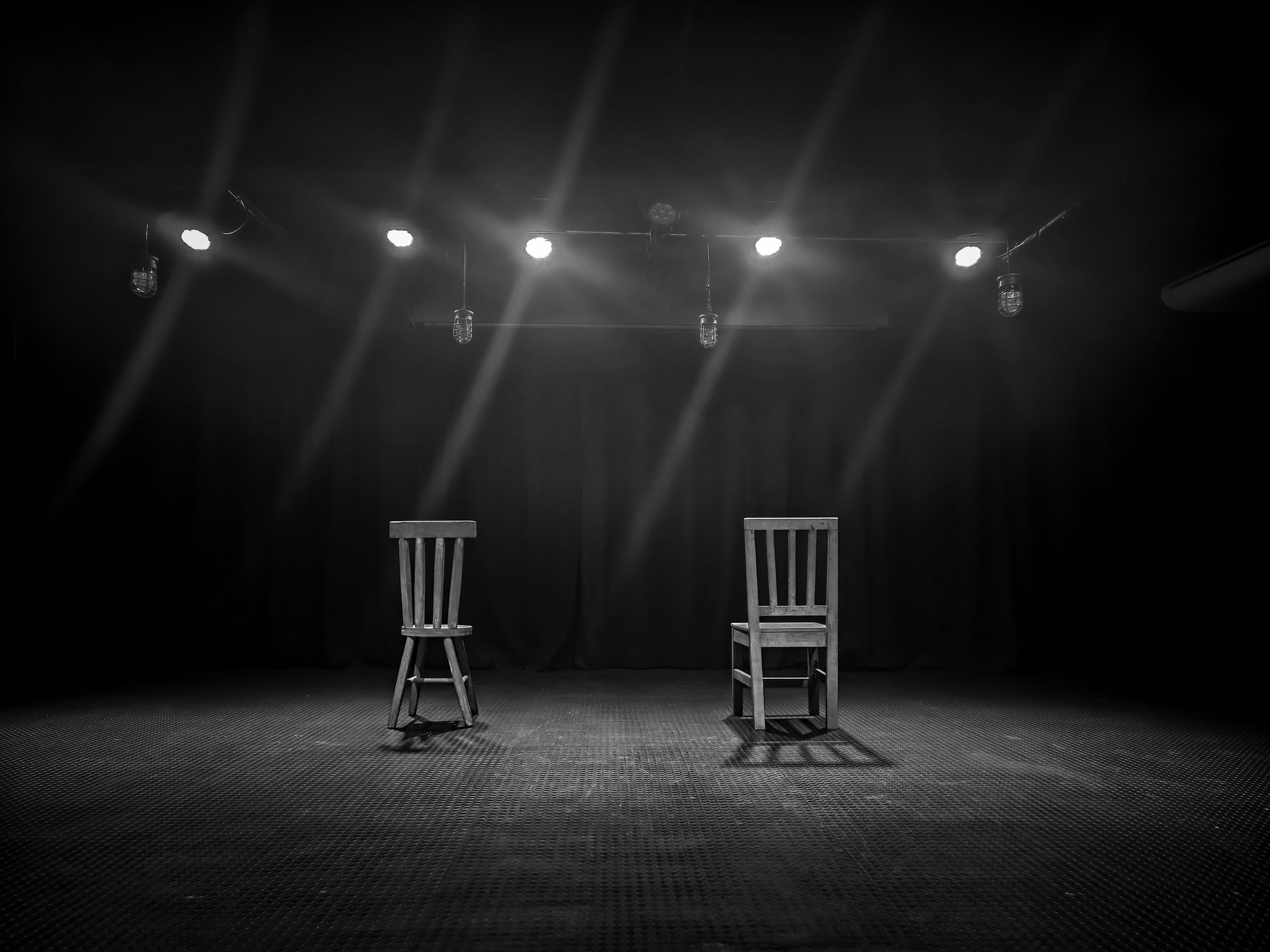 Two empty chairs on a dark stage under spotlights