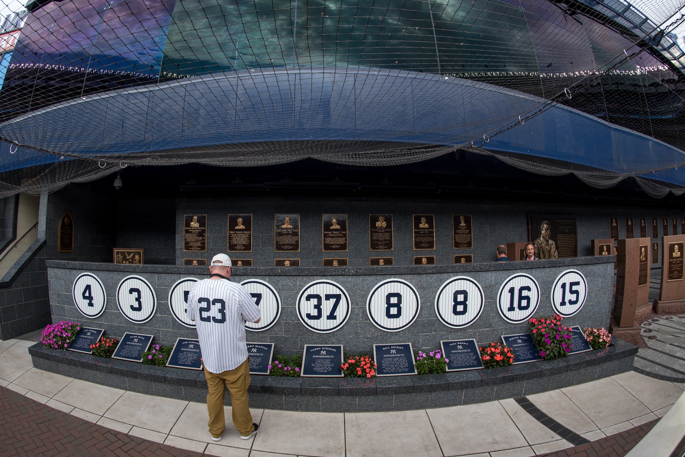 A fan in a number 23 jersey facing the wall of retired Yankees numbers in Monument Park