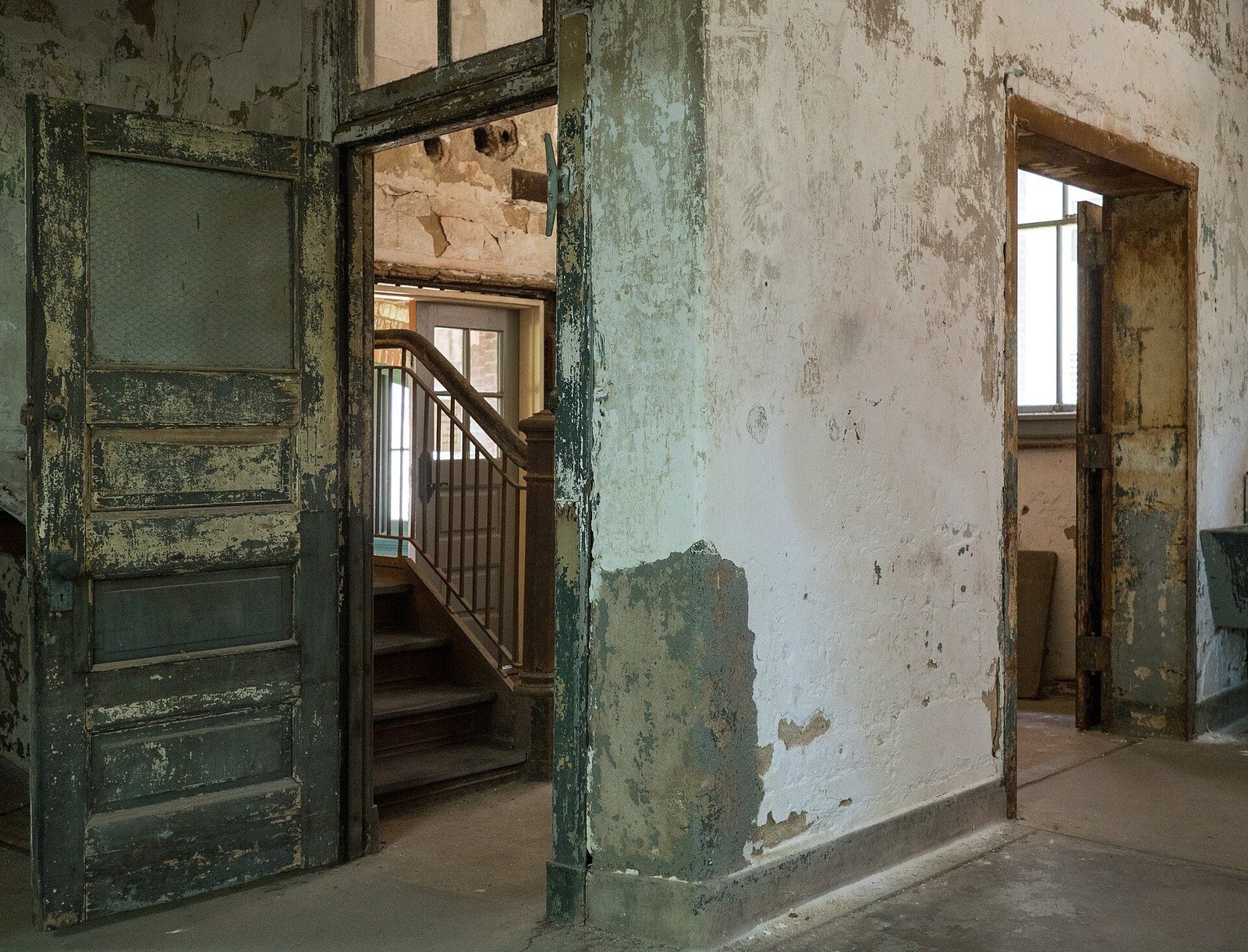 Peeling walls, a weathered wooden door and a stairway inside the unrestored Ellis Island Immigrant Hospital