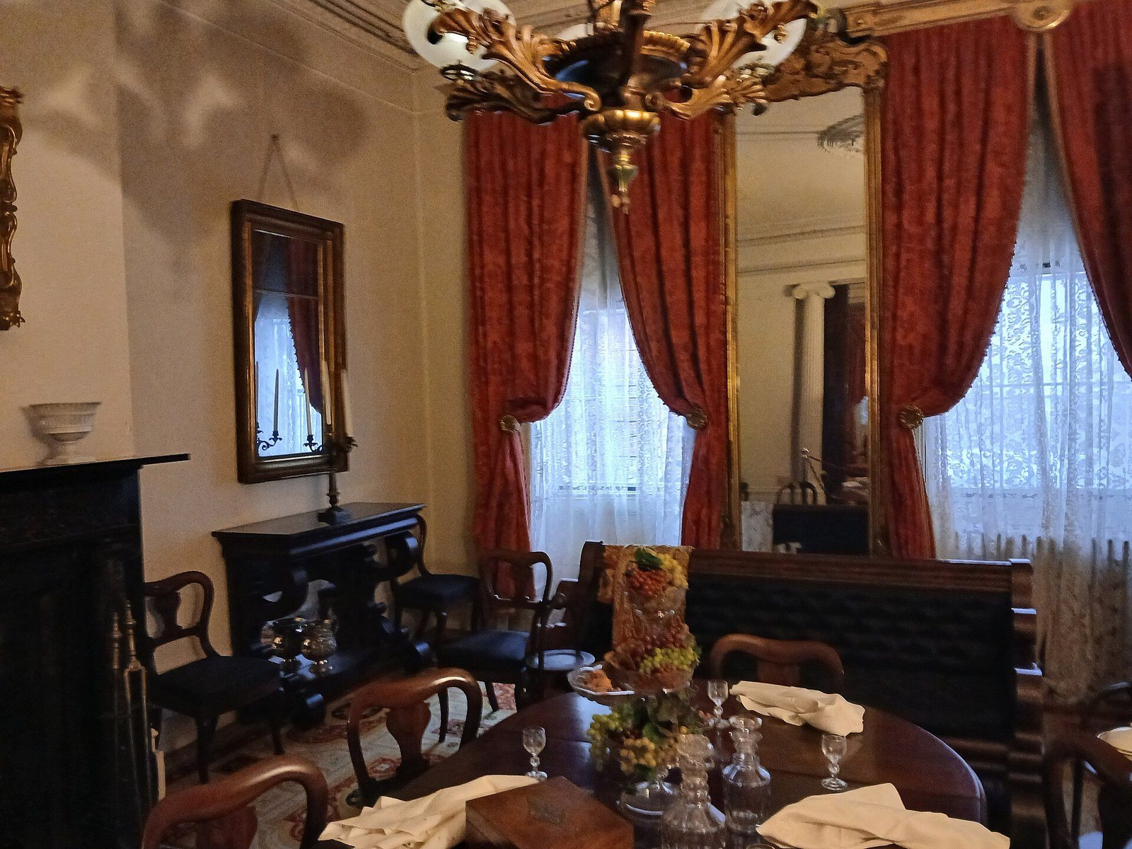 A first-floor room at the Merchant's House Museum set for dinner, with red drapes, a chandelier and period furniture
