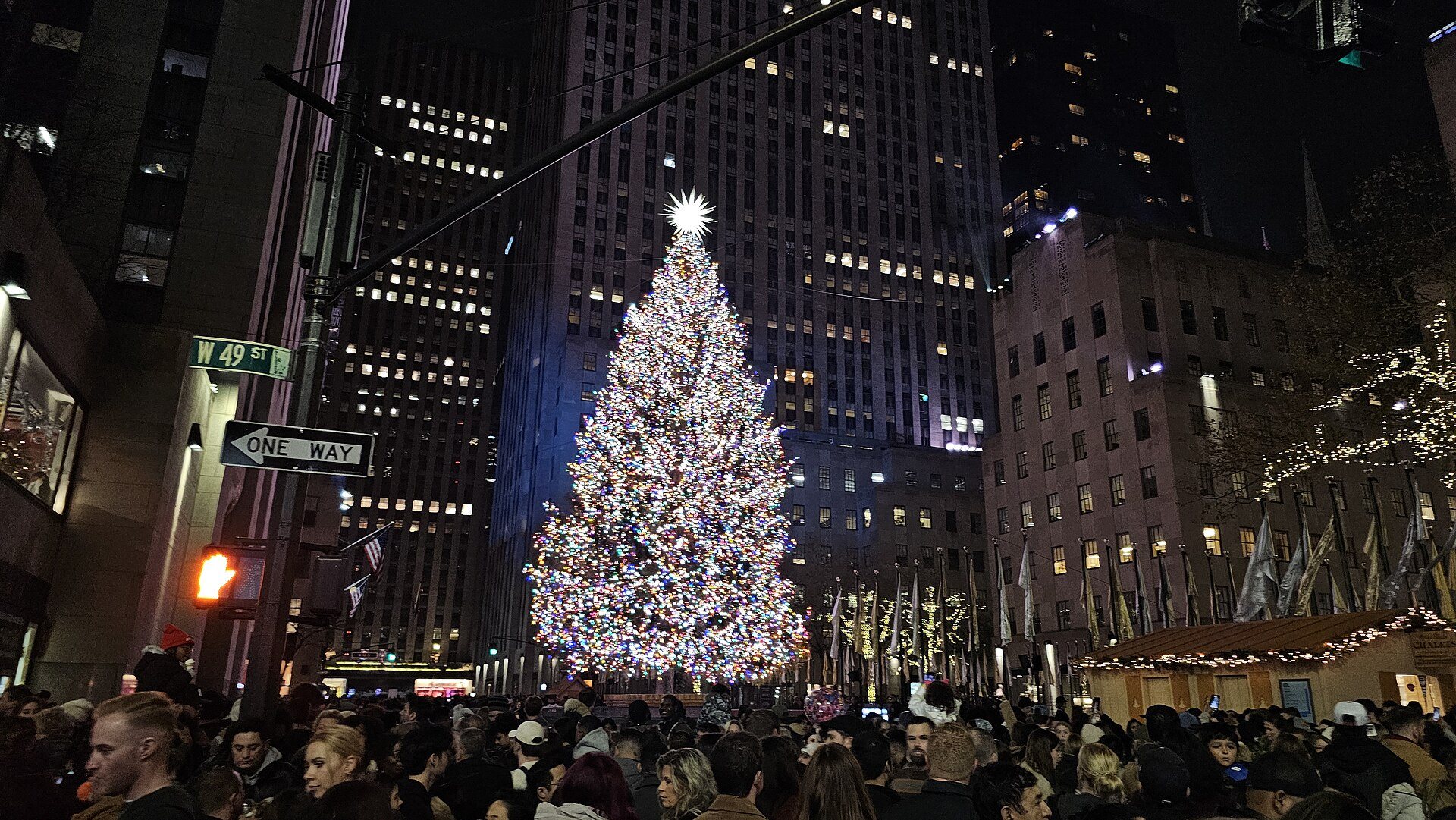 The Rockefeller Center Christmas tree lit at night above a crowd, with the tower of 30 Rockefeller Plaza behind