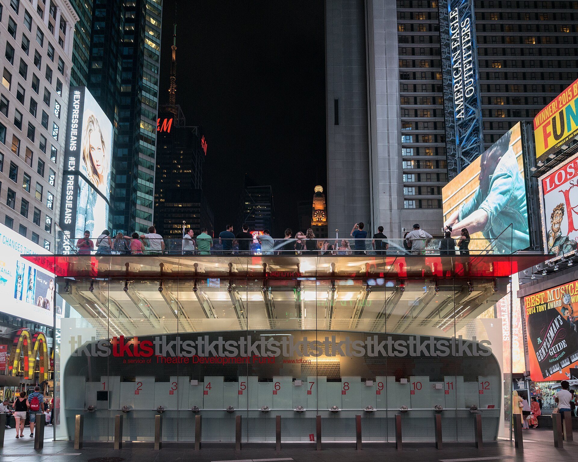 The TKTS booth under the red steps in Duffy Square, Times Square, with people seated on the steps