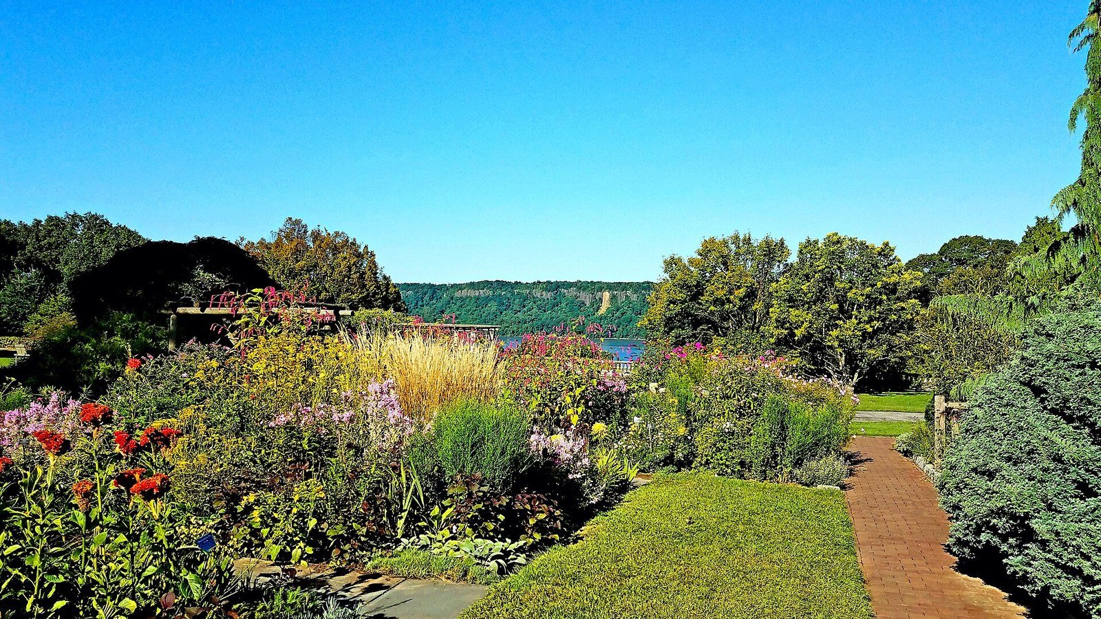 Flower borders in bloom at Wave Hill, with the Hudson River and the Palisades beyond