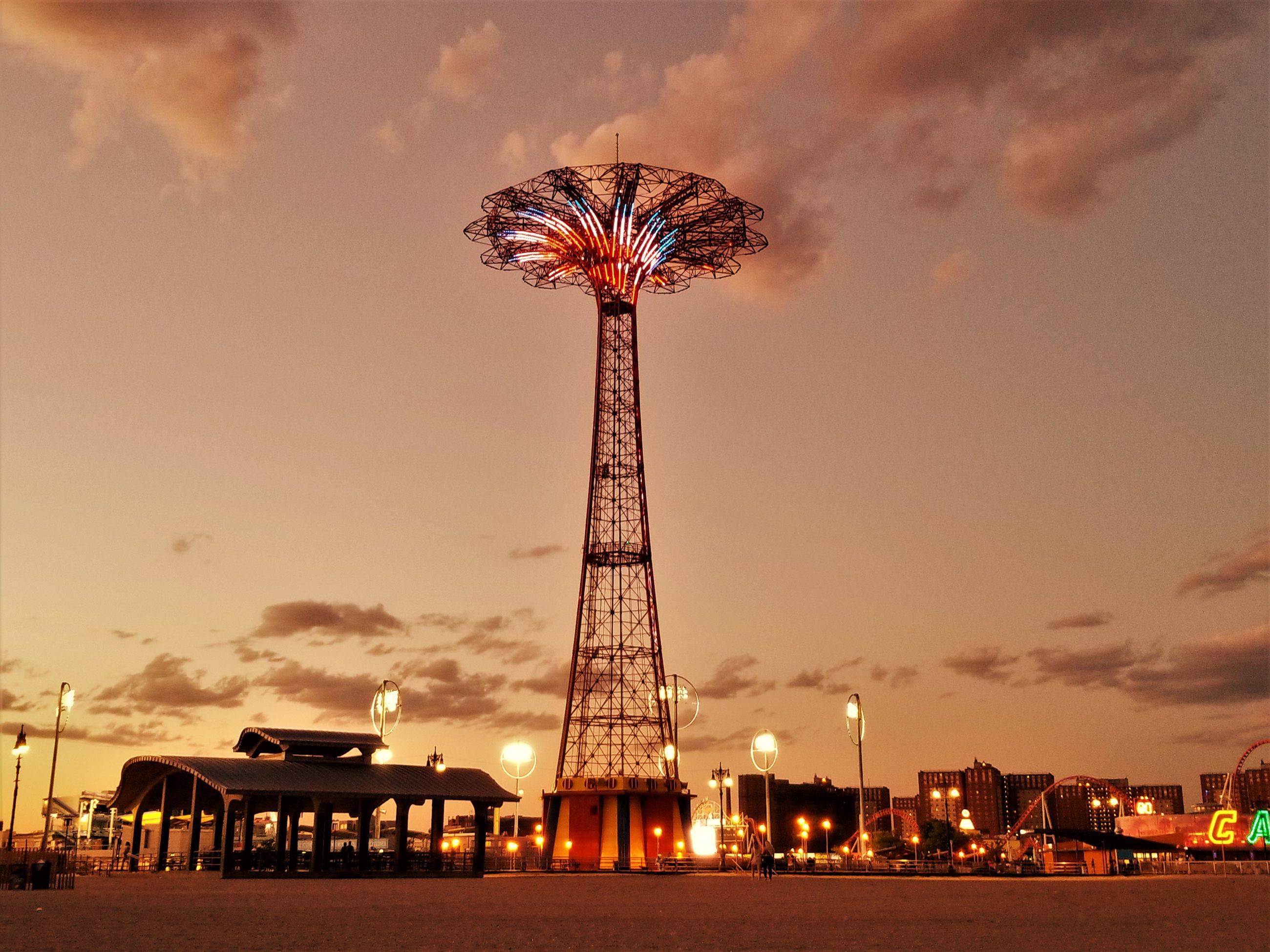Coney Island's Parachute Jump lit up against a sunset sky above the boardwalk