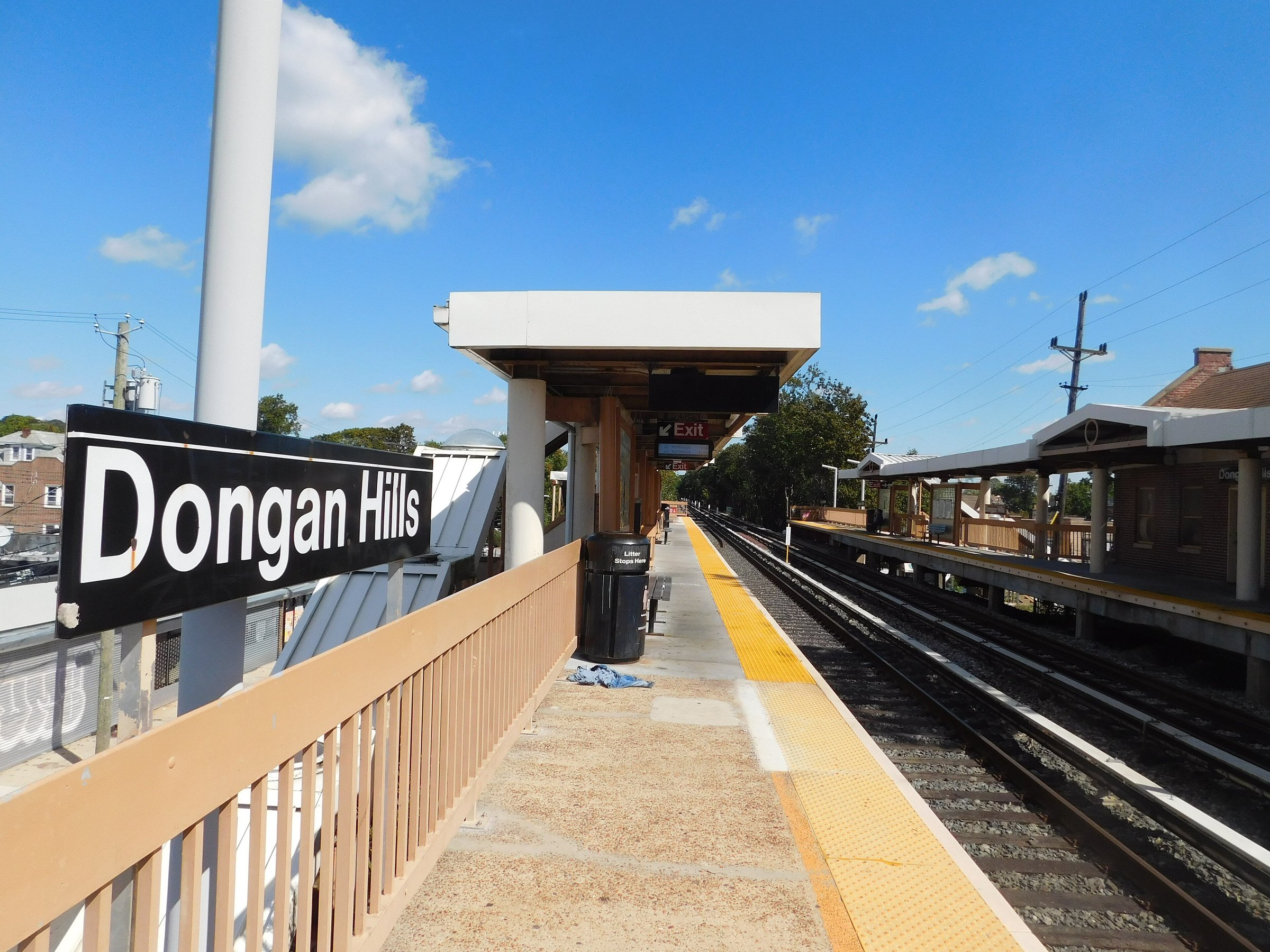 The Dongan Hills sign on the Staten Island Railway platform on a clear day, the tracks curving away past the station shelter