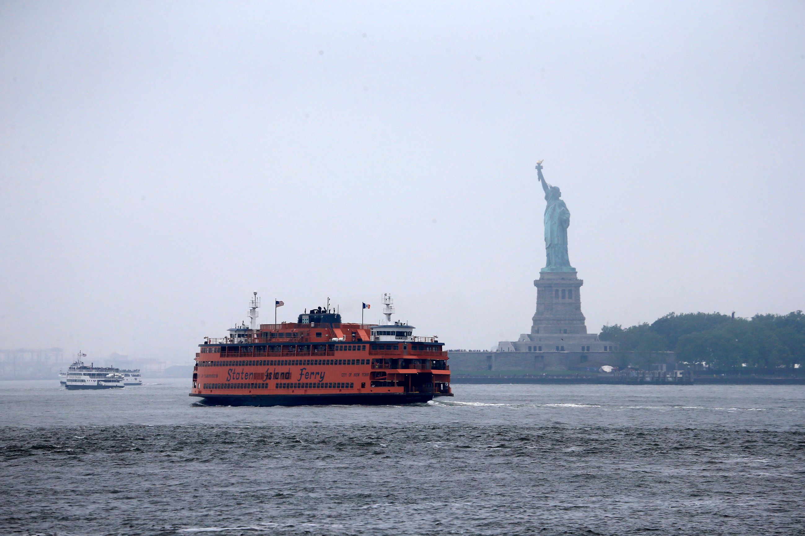 An orange Staten Island Ferry crossing the harbor past the Statue of Liberty on the run to St. George
