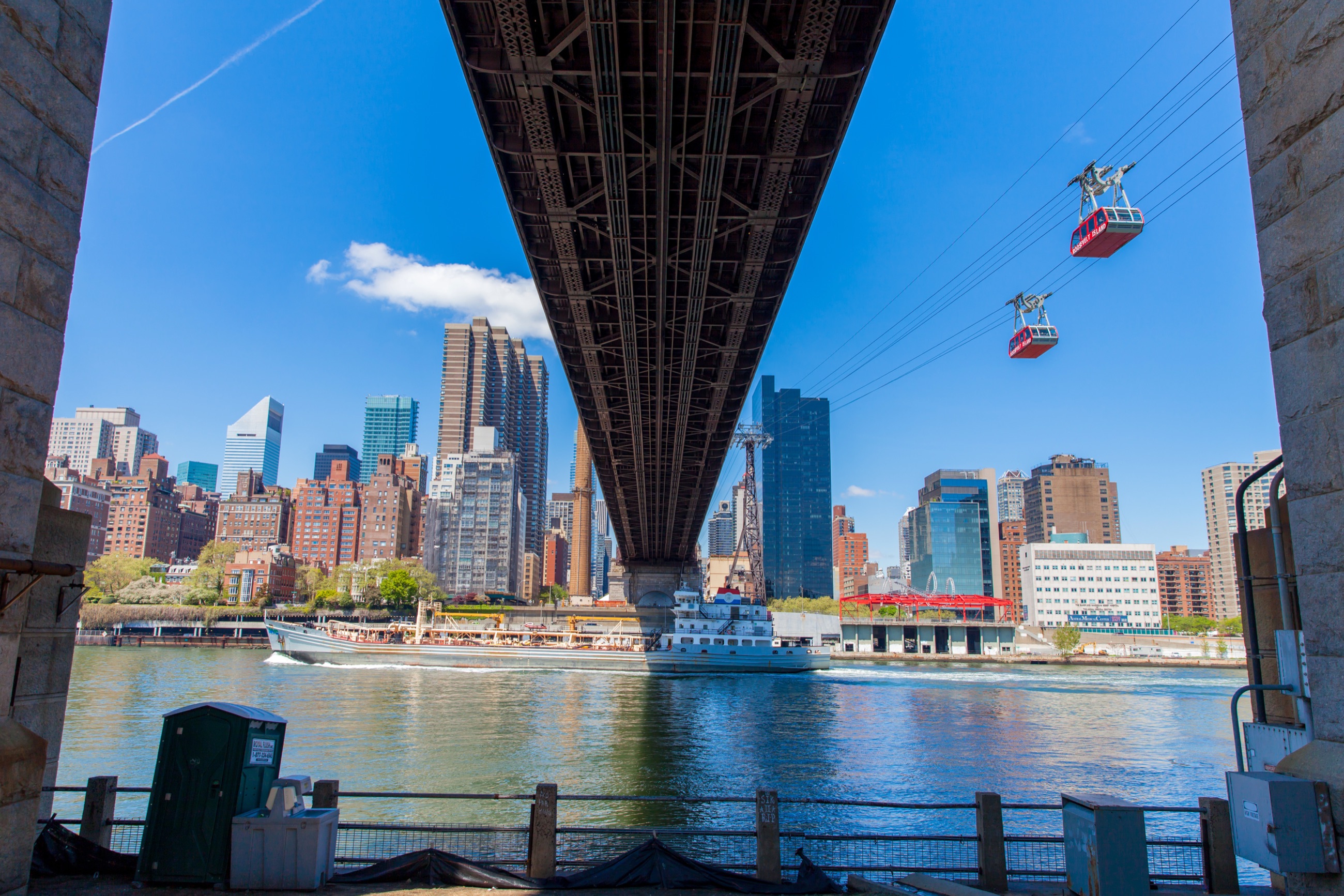 Two red Roosevelt Island tram cabins crossing the East River beside the Queensboro Bridge