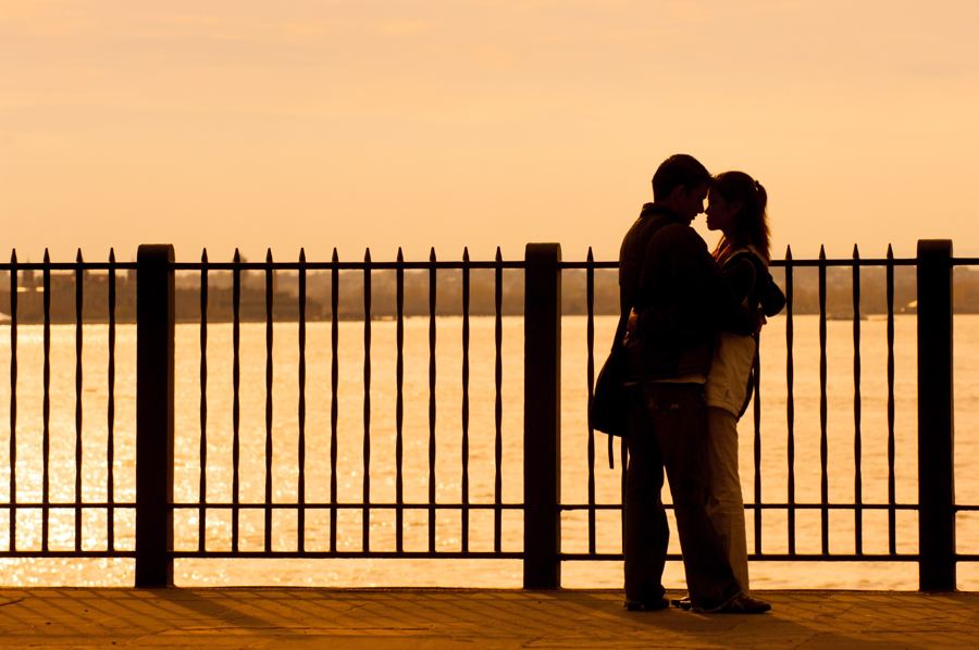 The lower Manhattan skyline and harbor seen across benches and railings on the Brooklyn Heights Promenade