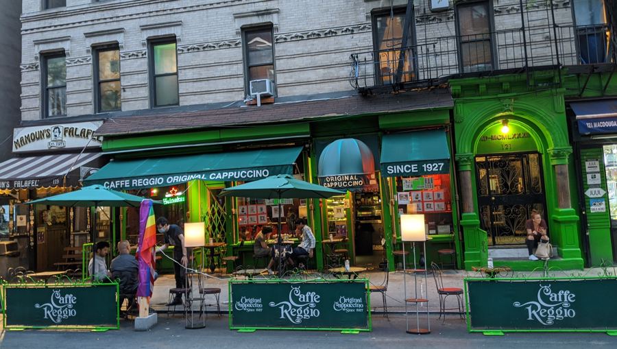 Caffe Reggio's green storefront and sidewalk tables on MacDougal Street at dusk