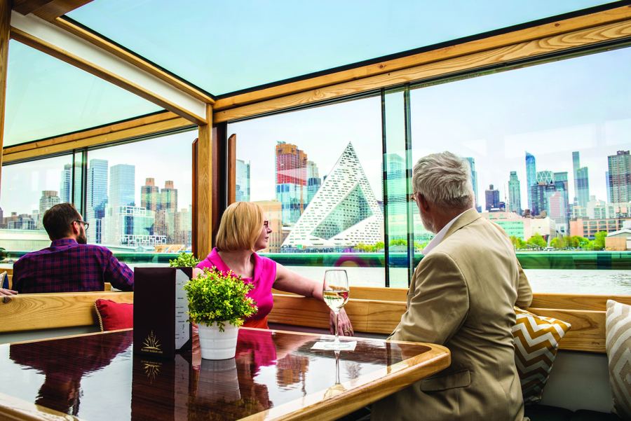 Passengers at a window table aboard a Classic Harbor Line yacht, the Manhattan skyline sliding by