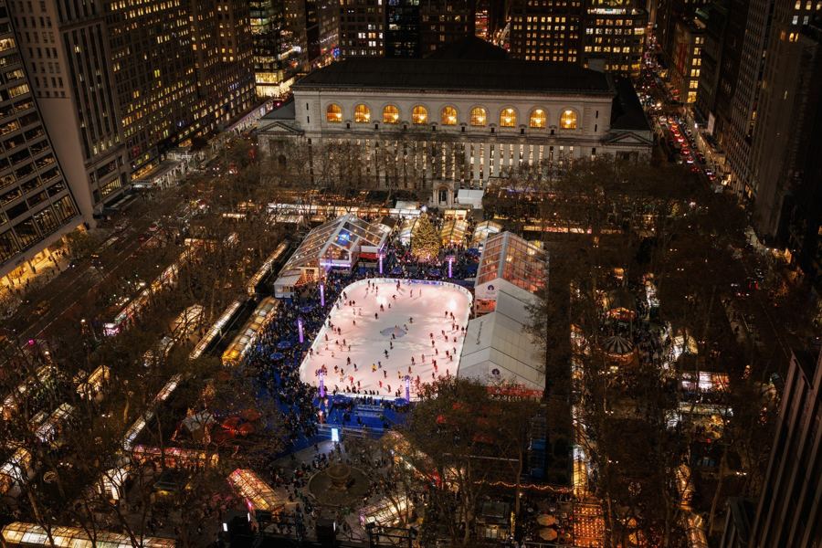 Skaters circling the rink at Bryant Park's Winter Village beneath Midtown towers, snowflake umbrellas in the foreground