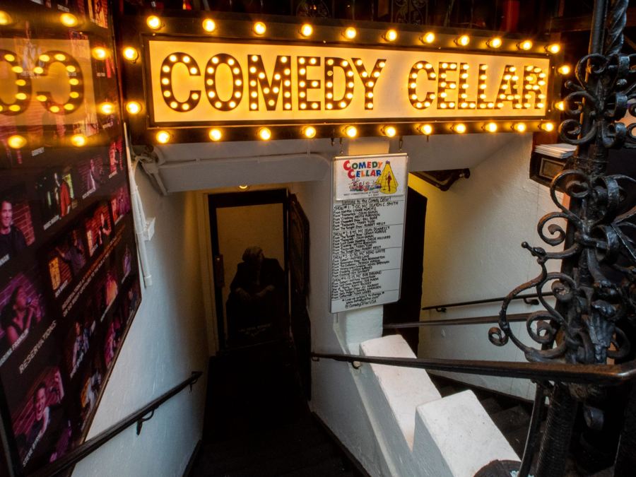 The Comedy Cellar's bulb-lit sign above its MacDougal Street stair entrance