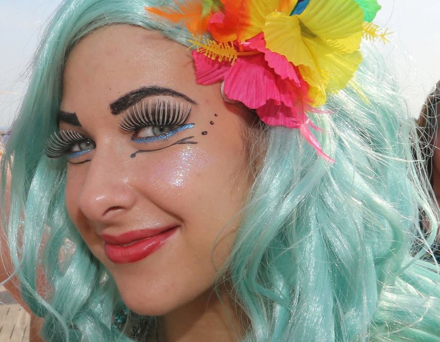 A smiling mermaid with seafoam hair, a hibiscus crown and glittered lashes at the Mermaid Parade