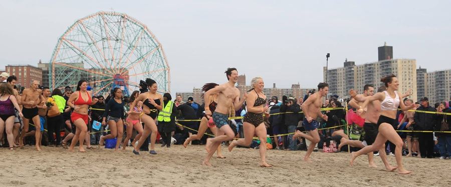 Swimmers sprinting down the beach under the Wonder Wheel at the Polar Bear Plunge