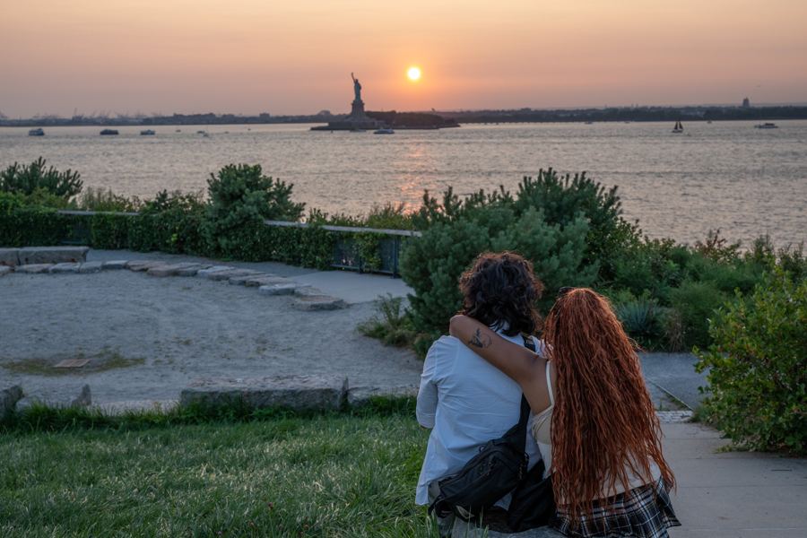 A couple watching the sun set behind the Statue of Liberty from Governors Island