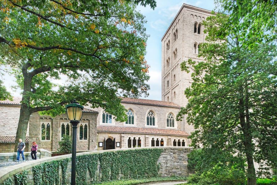 The Met Cloisters' stone tower and arcades above an ivy-covered wall and garden path