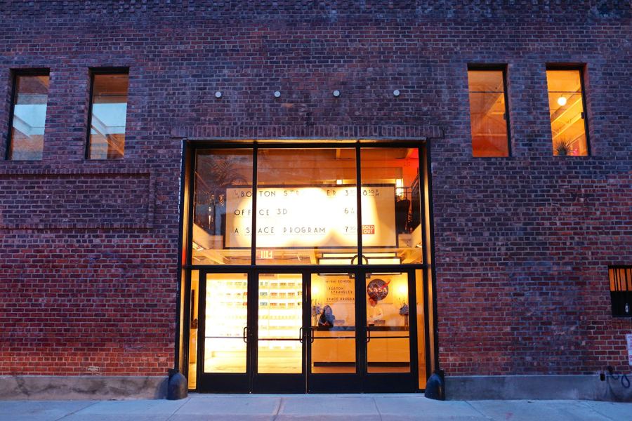 Metrograph's brick facade at dusk, its tall entrance windows lit warm gold