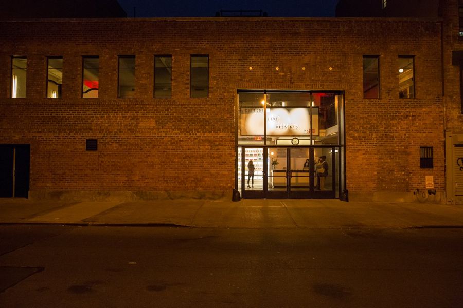 Metrograph's brick building and glowing doors on a quiet street at night