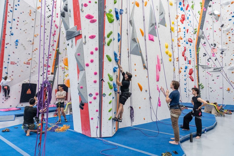 Climbers and belayers at the tall rope walls of Movement Gowanus