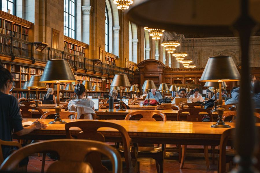Readers at the lamp-lit tables of the New York Public Library's reading room