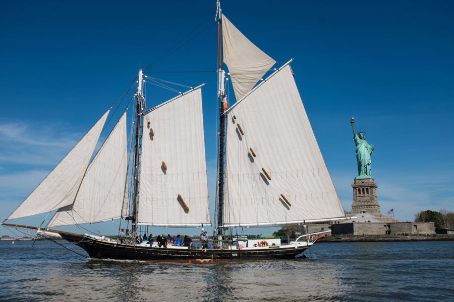 The 1885 schooner Pioneer under full sail in New York Harbor, the Statue of Liberty behind