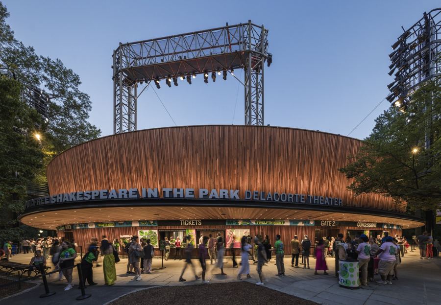 The renovated Delacorte Theater's curved wood facade at twilight, Free Shakespeare in the Park lettered over the entrance