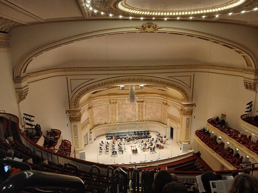 Inside the Isaac Stern Auditorium at Carnegie Hall, with an orchestra on stage and tiers of red seats, January 2026
