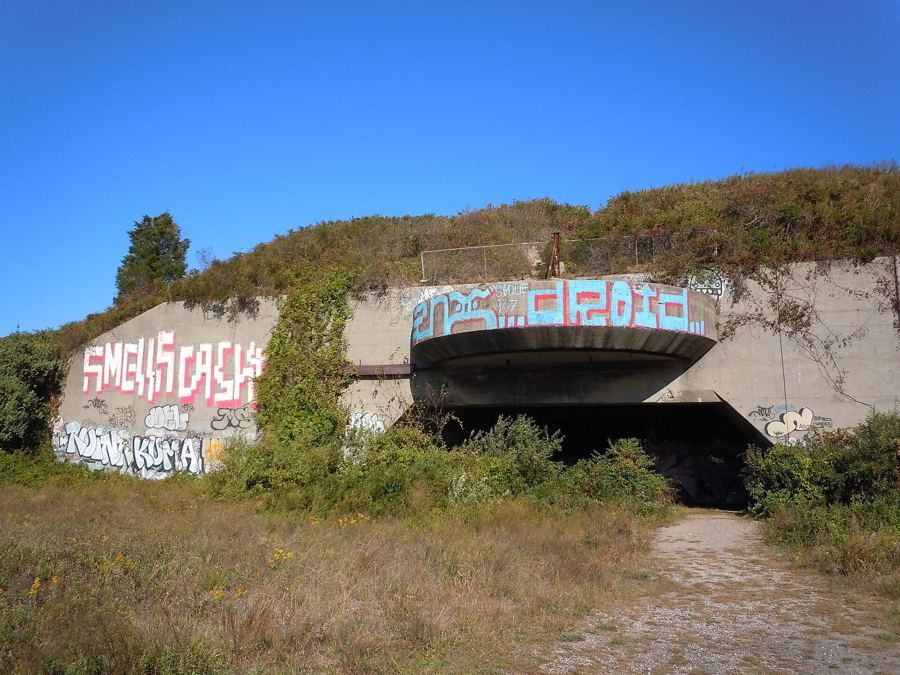 The graffitied concrete casemate of a 16-inch gun battery at Fort Tilden, half-buried in grassy dunes