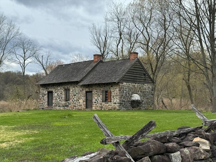 The fieldstone Christopher House at Historic Richmond Town, set in a grassy field behind a split-rail fence