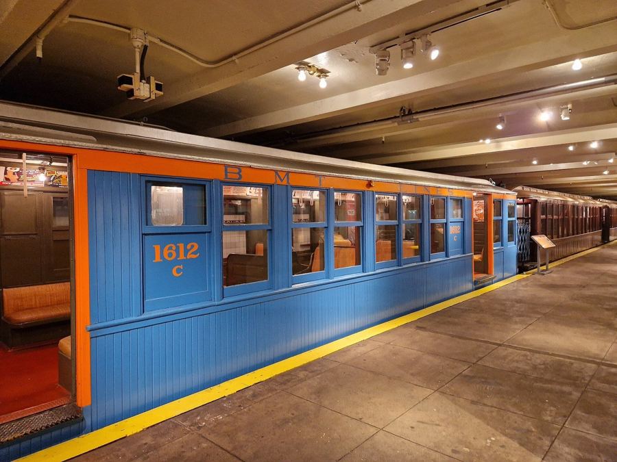 A vintage blue-and-orange subway car parked at the platform inside the New York Transit Museum