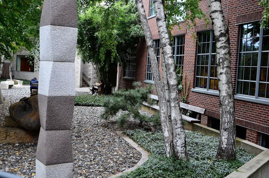 The sculpture garden at the Noguchi Museum, with a stone column, birch trees and gravel beds beside the brick gallery