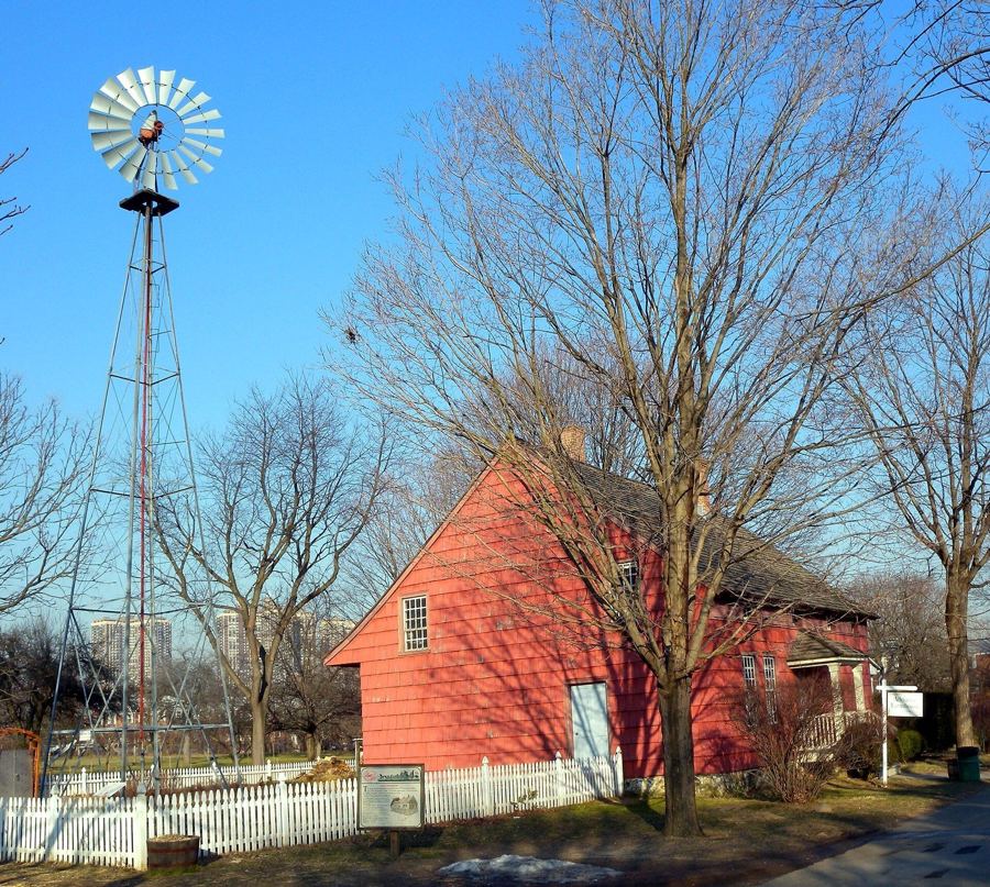 The farm's historic red farmhouse and a windmill under a clear winter sky at the Queens County Farm Museum