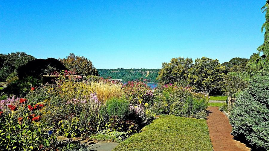Flower borders in bloom at Wave Hill, with the Hudson River and the Palisades beyond