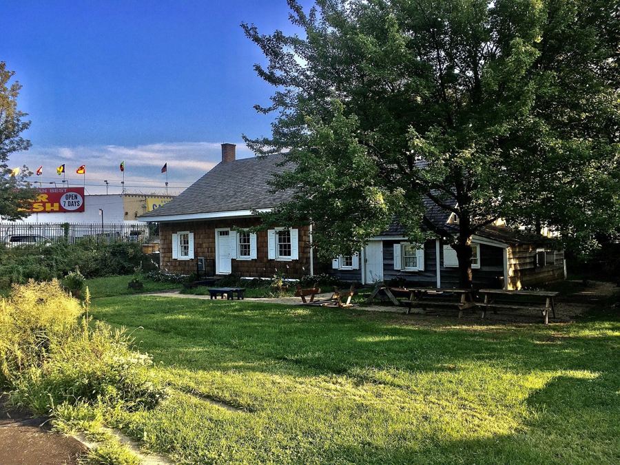 The low, shingled Wyckoff farmhouse behind a green lawn and garden in East Flatbush
