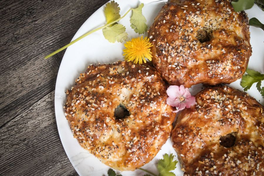 Everything bagels piled on a white plate with small yellow and pink flowers