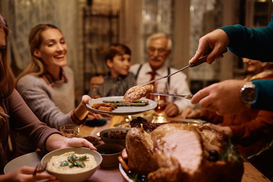 Serving slices of roast turkey onto plates at a family Thanksgiving dinner