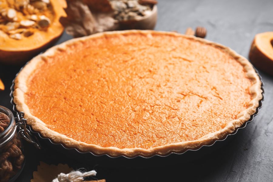 A whole pumpkin pie in a tart pan beside halved pumpkins and pecans