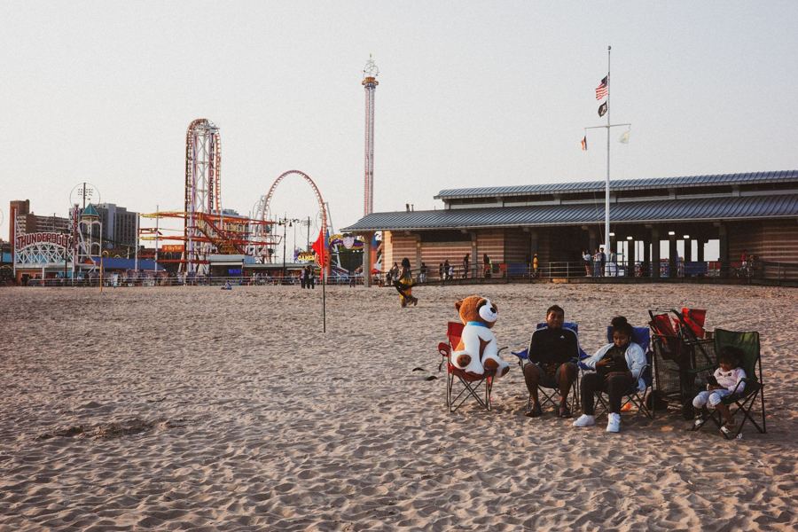 Families on the beach at Coney Island with the rides behind