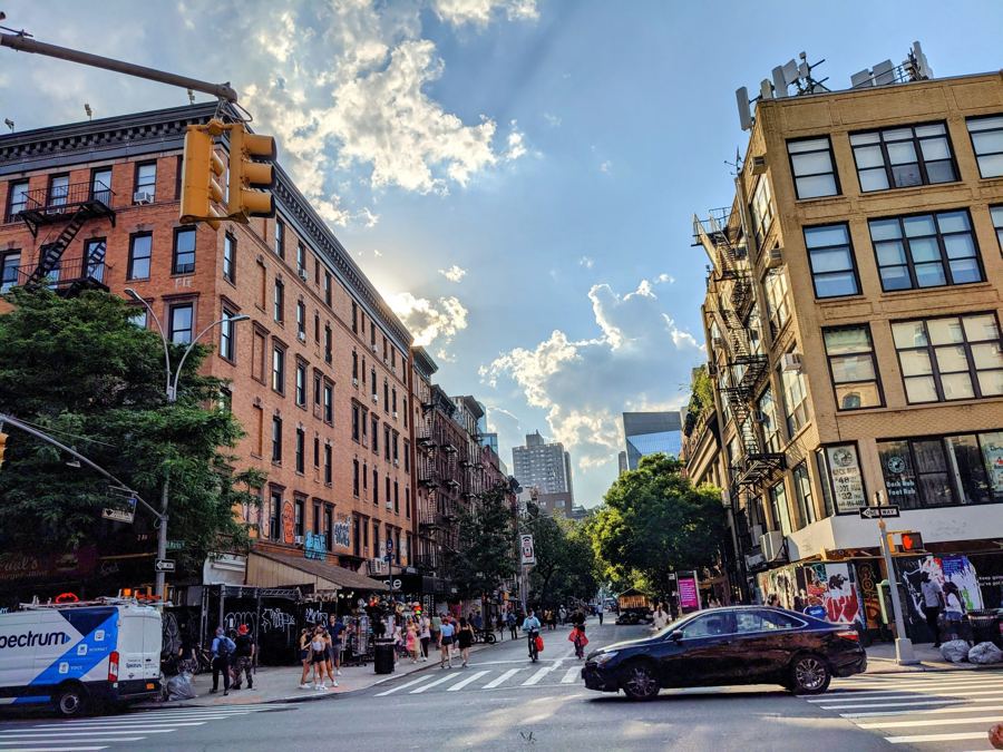 St. Marks Place seen from Second Avenue in the East Village, with tenement buildings, shopfronts and passersby under a bright summer sky.