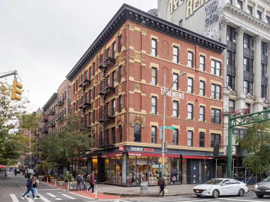 A red-brick tenement with black fire escapes and the Tenement Museum shop at street level on the corner of Orchard and Delancey Streets.