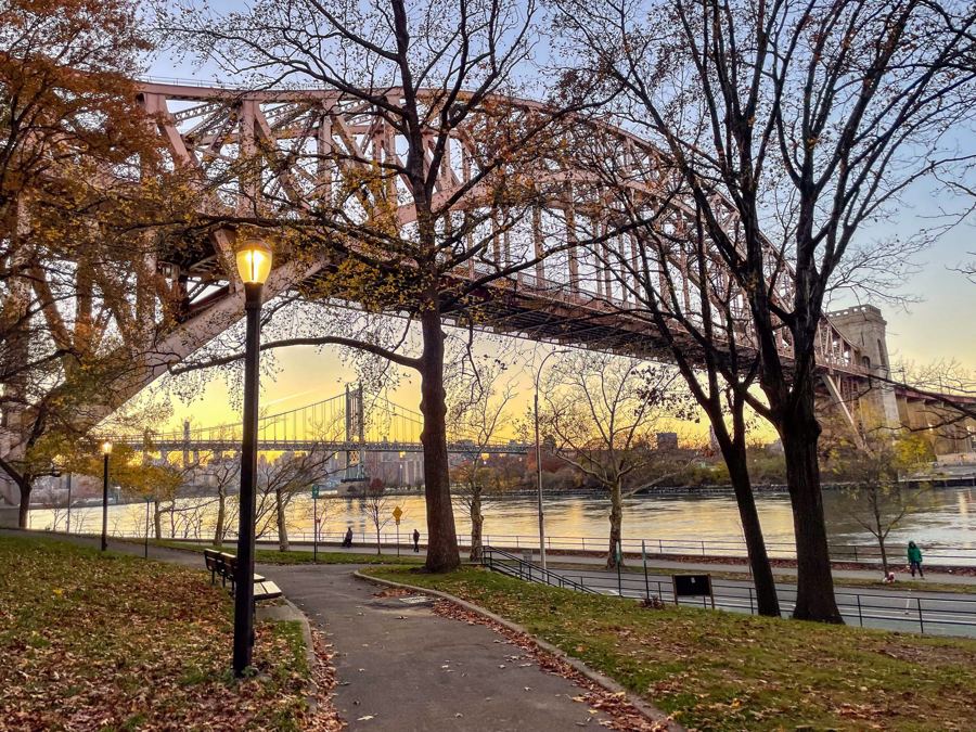 The Hell Gate Bridge's arch seen through the trees of Astoria Park at golden hour